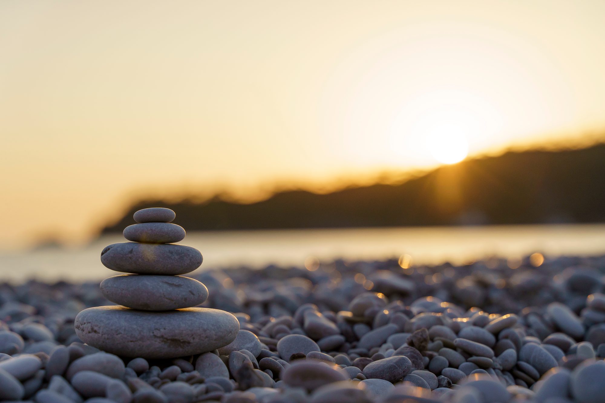 A balanced stack of smooth pebbles on a calm Devon beach at golden sunset — a quiet symbol of feeling steady and at peace